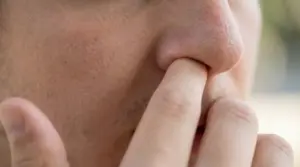 Persona si infila un dito nel naso in primo piano