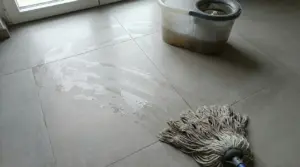 Pavimento bagnato con aloni e mocio accanto a un secchio con acqua sporca
