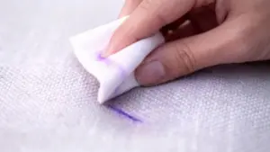 Mano che tampona una macchia viola su un divano chiaro con un panno bianco