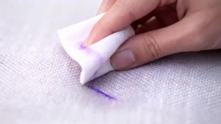 Mano che tampona una macchia viola su un divano chiaro con un panno bianco