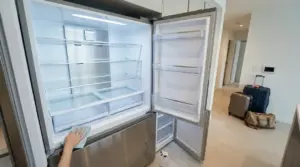 Una mano pulisce un frigorifero vuoto con valigie pronte vicino all'ingresso