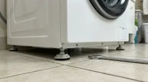 Piedini regolabili di una lavatrice su un pavimento piastrellato con una chiave inglese a terra