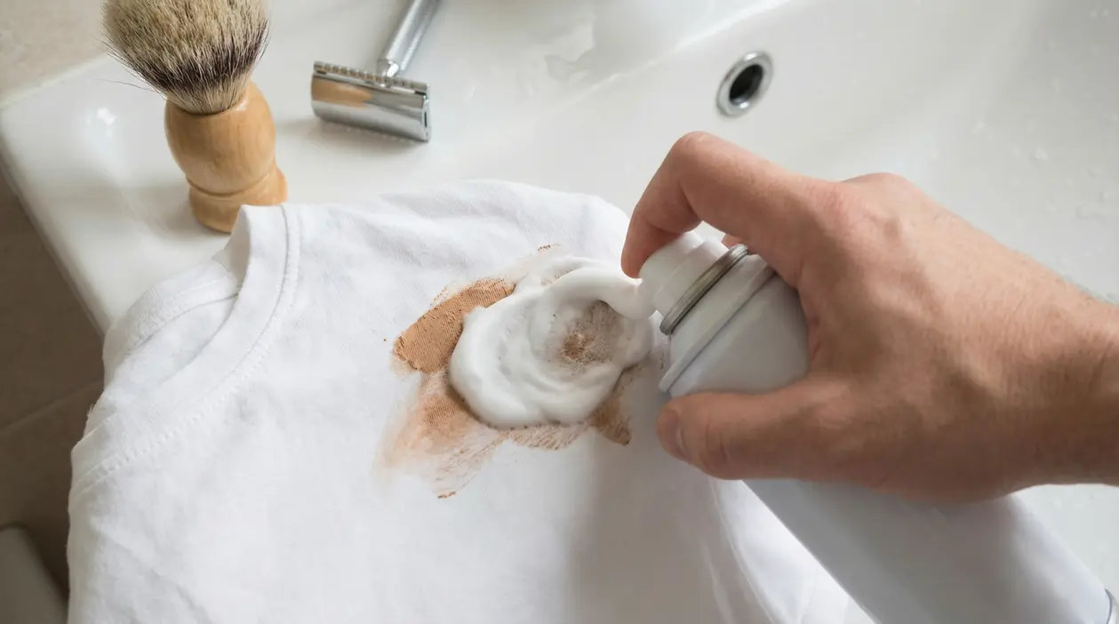 Mano applica schiuma da barba su una maglietta bianca macchiata di trucco