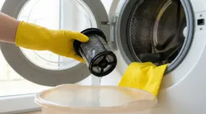 Mano con guanto giallo che pulisce il filtro di una lavatrice con acqua.