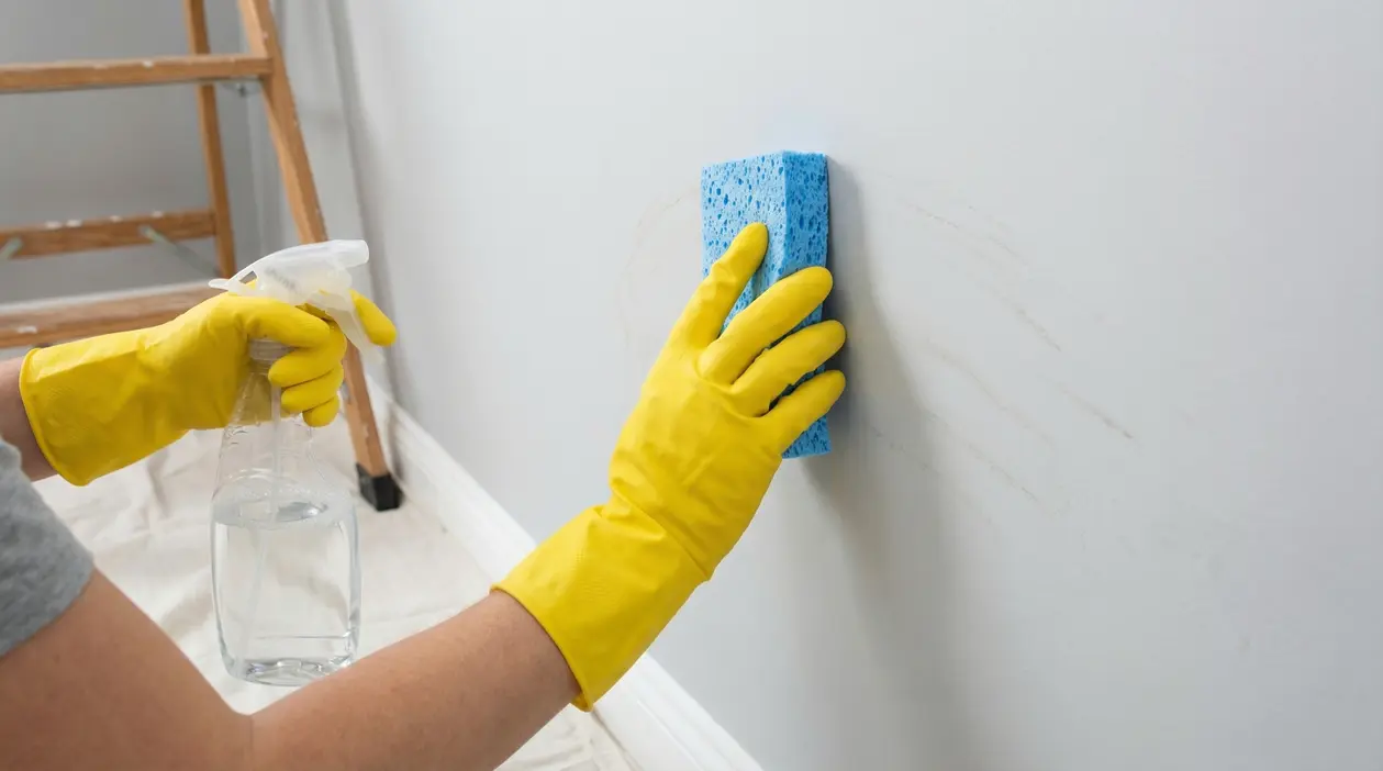 Mani con guanti gialli puliscono una parete con una spugna e uno spray