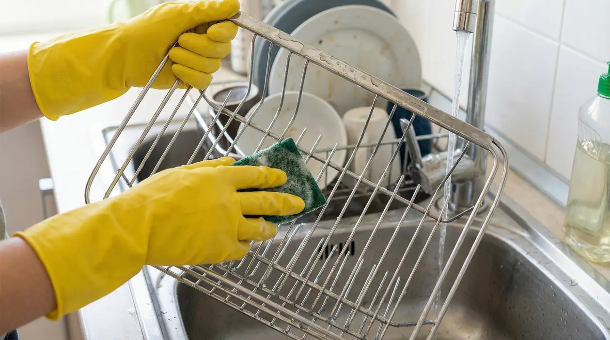 Persona con guanti gialli pulisce uno scolapiatti in acciaio sopra un lavandino