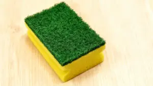 Spugna da cucina con lato abrasivo verde su sfondo in legno chiaro