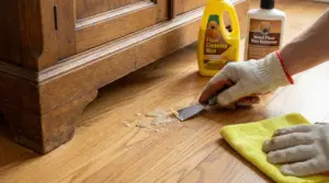 Una mano con guanto rimuove della cera da un pavimento in legno con una spatola