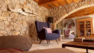 Poltrona blu con cuscino rosa in un soggiorno rustico con pareti in pietra e mobili in legno