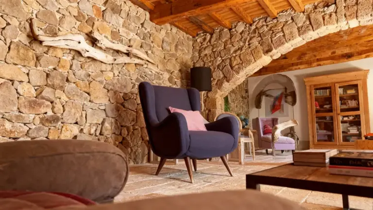 Poltrona blu con cuscino rosa in un soggiorno rustico con pareti in pietra e mobili in legno