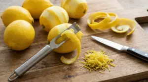 Limoni interi e sbucciati con scorza grattugiata e strumenti da cucina su un tagliere