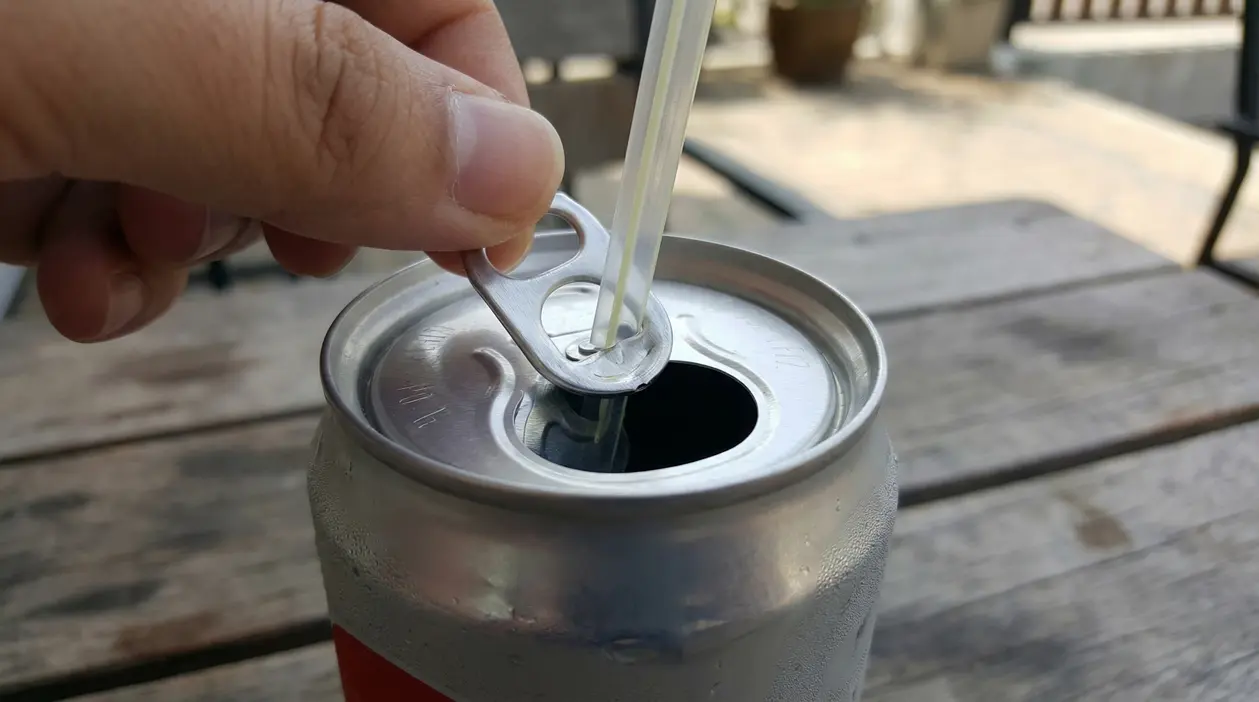 Una mano inserisce una cannuccia nella linguetta di una lattina di bibita